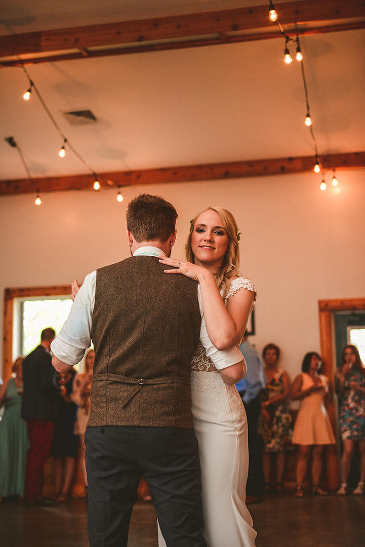 a man and a woman dancing at a wedding reception during the first dance with warm light bulbs hanging from the rafters of a old barn