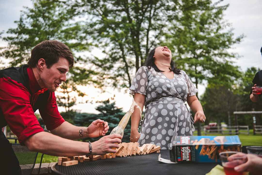 a man catching a beer as it spills while playing jenga outside at the All Season Orchard as a woman laughs