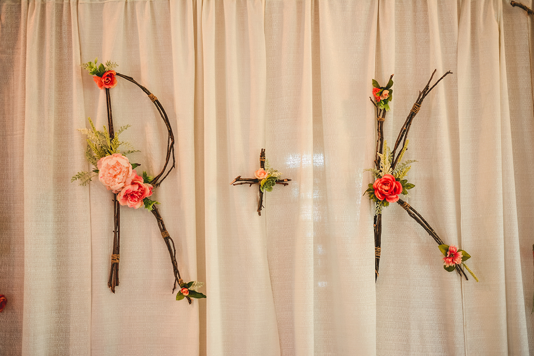 wooden sticks weaved into the initials of the bride and groom with flowers laid across them