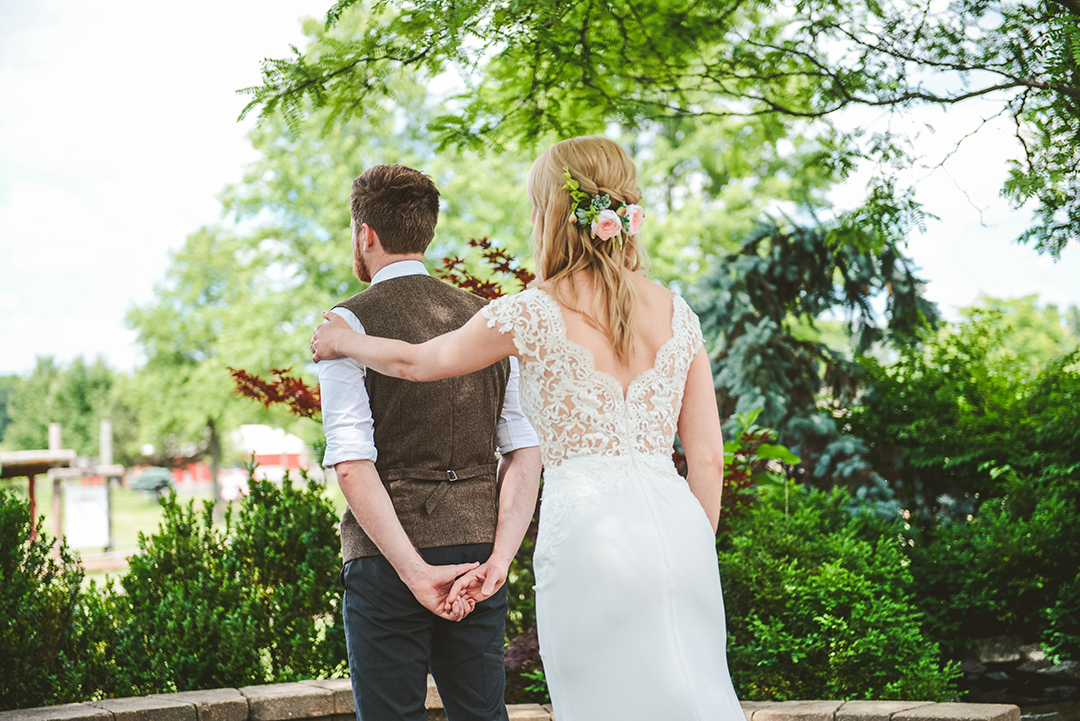 a woman touching her grooms shoulder during their first look under trees