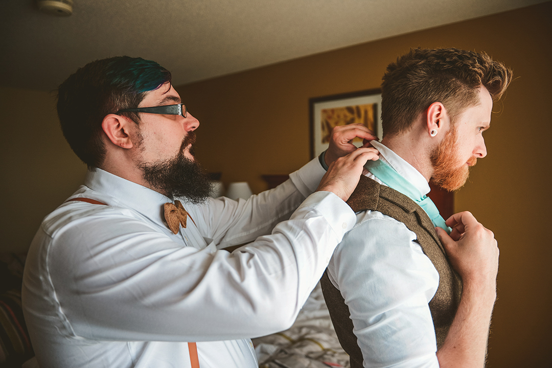 the best man fixing the grooms tie in a warmly lit hotel room