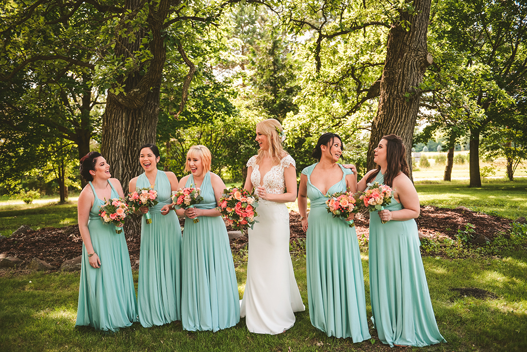 a group of bridesmaids laughing with the bride in the woods at an apple orchard