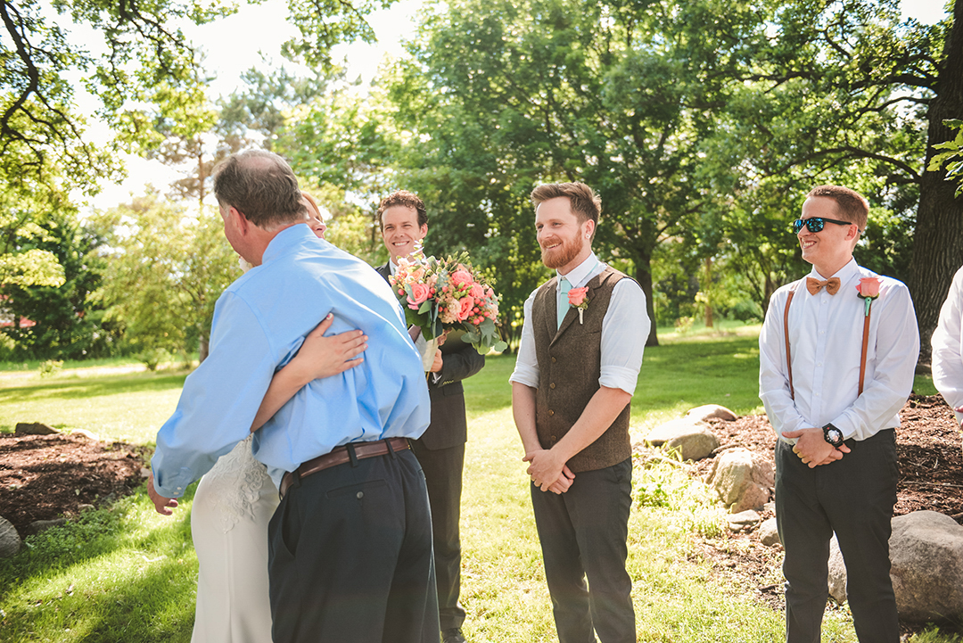 the groom smiling as the brides father hugs her goodbye at a wedding ceremony