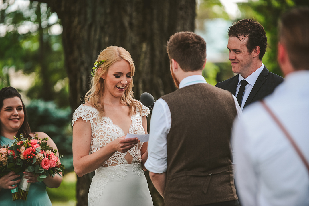 a bride laughing as she reads her vows to her groom as everyone laughs in the background