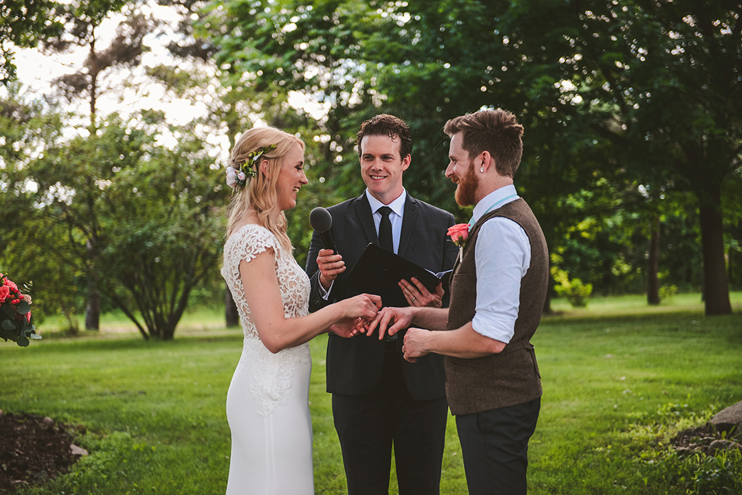 a husband and wife laughing as they exchange rings at a wooded orchard in Woodstock