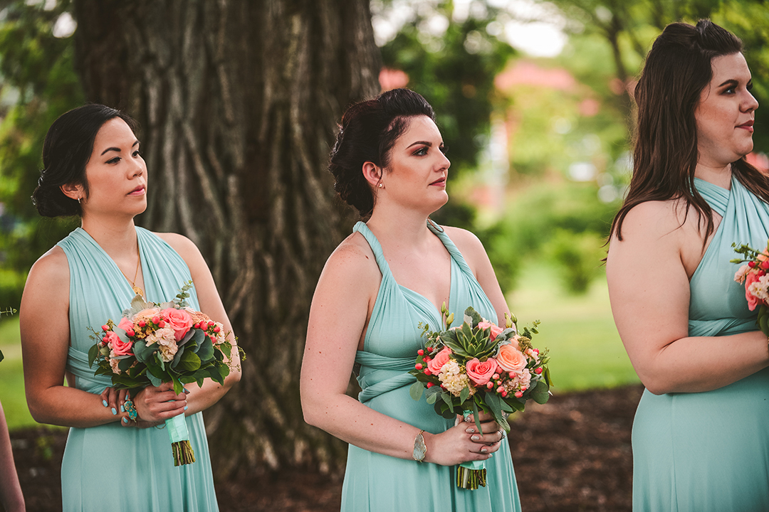 bridesmaids in blue dresses holding their bouquets as they watch the bride and groom say their vows at the All Season Orchard