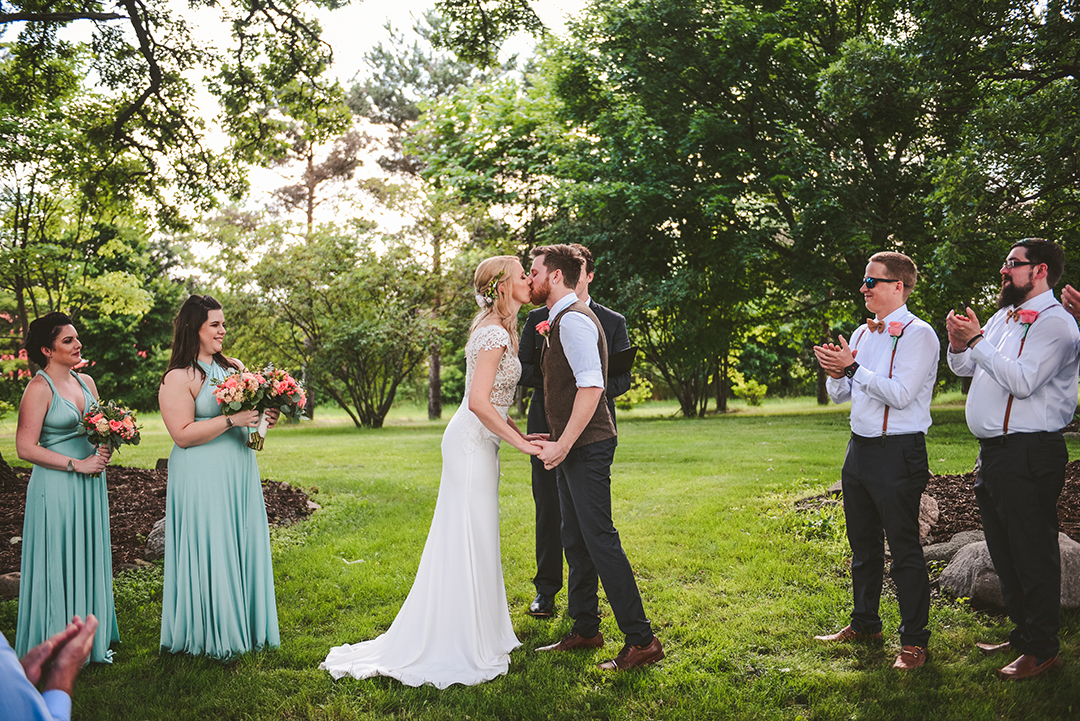 a bride and groom kissing for the first time at their wedding at the All Season Orchard as their bridal party smiles and claps