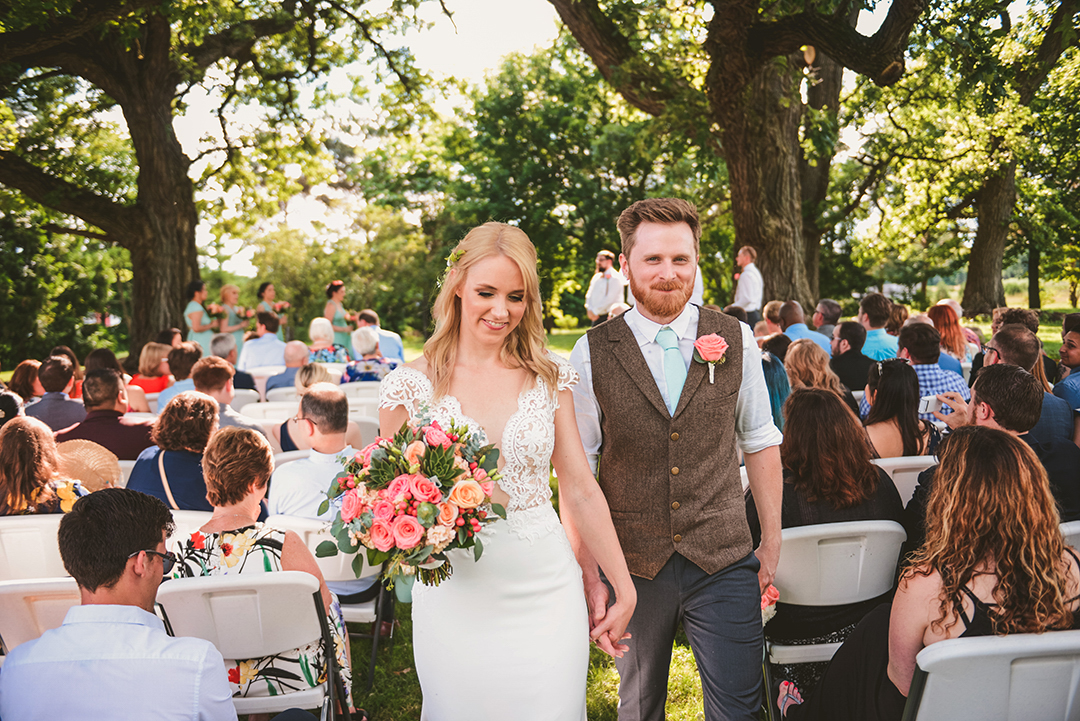 a bride and groom walking down the aisle after being married under two large oak trees at the All Season Orchard