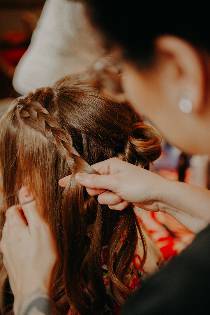 a hair stylist bradding the brides hair before the ceremony