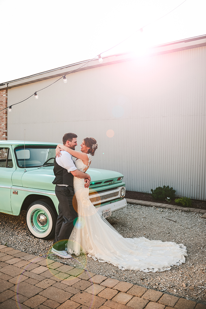 the bride and groom standing in front of an old truck at Warehouse 109 with a flair in the background