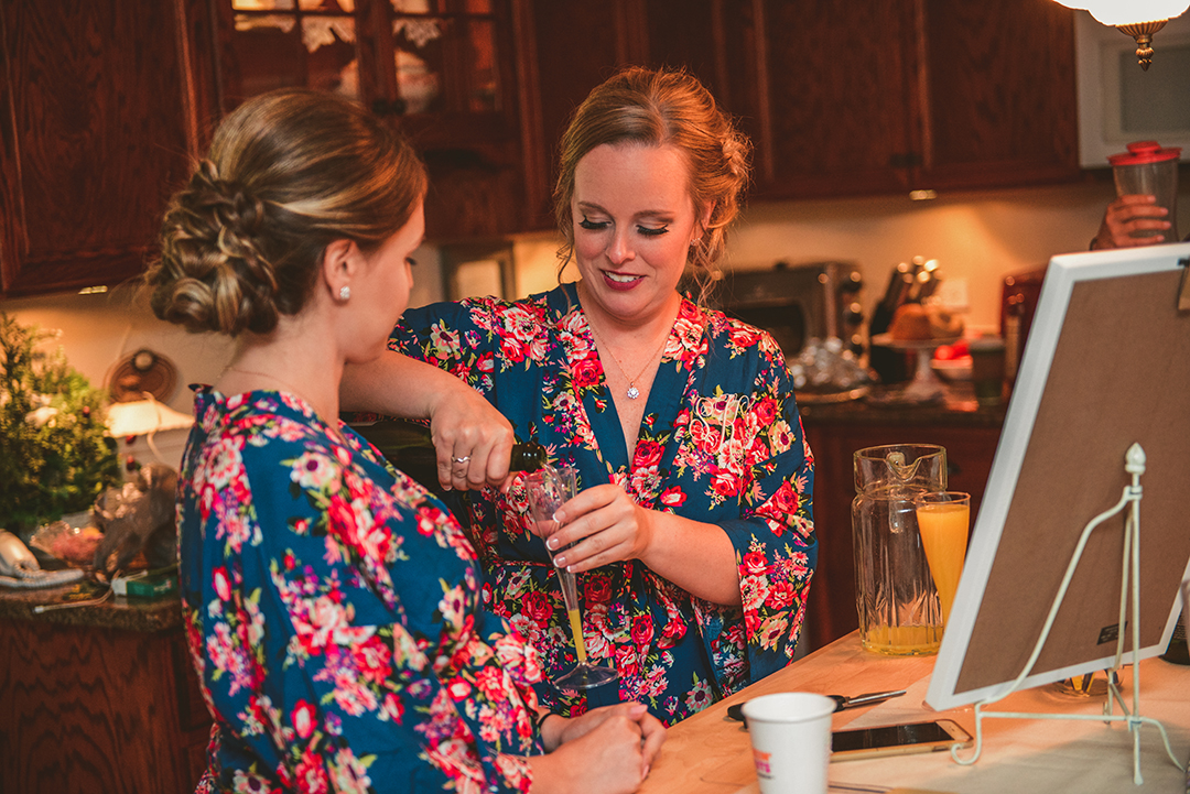 the maid of honor pouring a drink for a bridesmaid on the wedding day morning