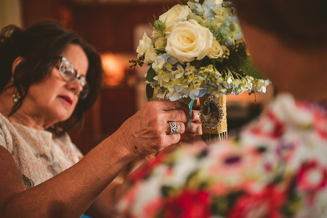 the bride and her mom putting an emblem on her bouquet before the wedding ceremony