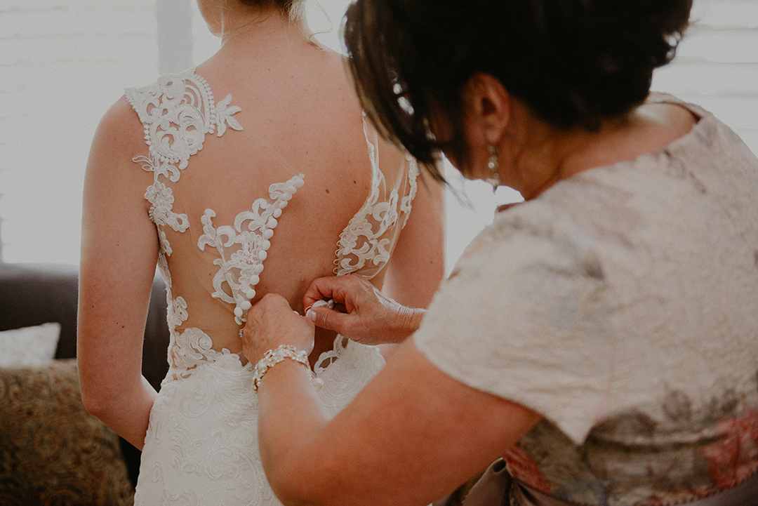 the brides mom buttoning up her dress before her wedding