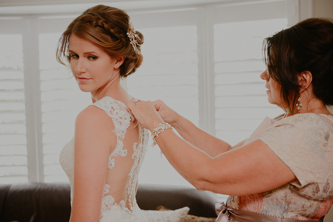 the bride looking back as her mom buttons up her dress