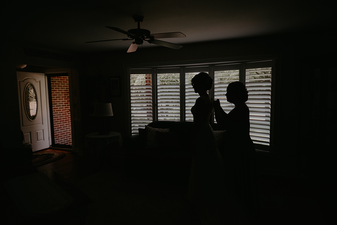 a silhouette of a bride and her maid of honor putting on the dress