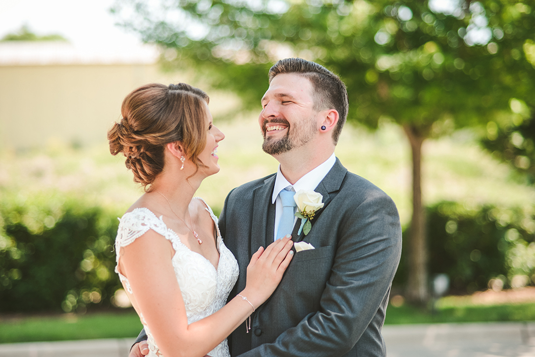 a groom laughing as his wife says something to him outside in the sun