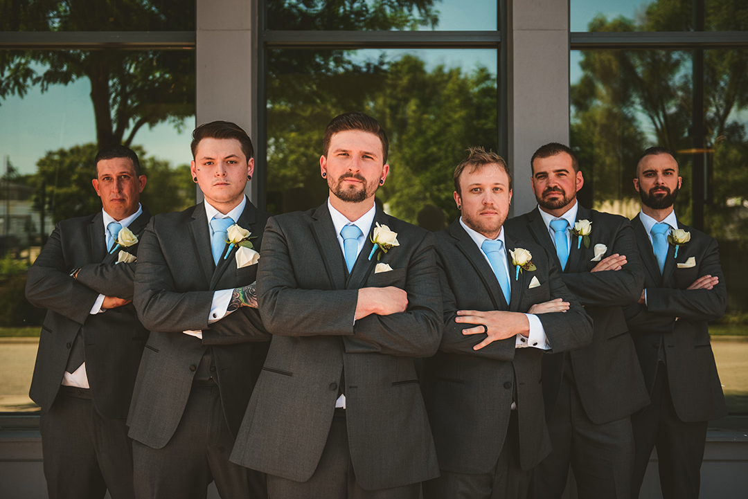 The groomsman standing in a V with their arms crossed looking serious