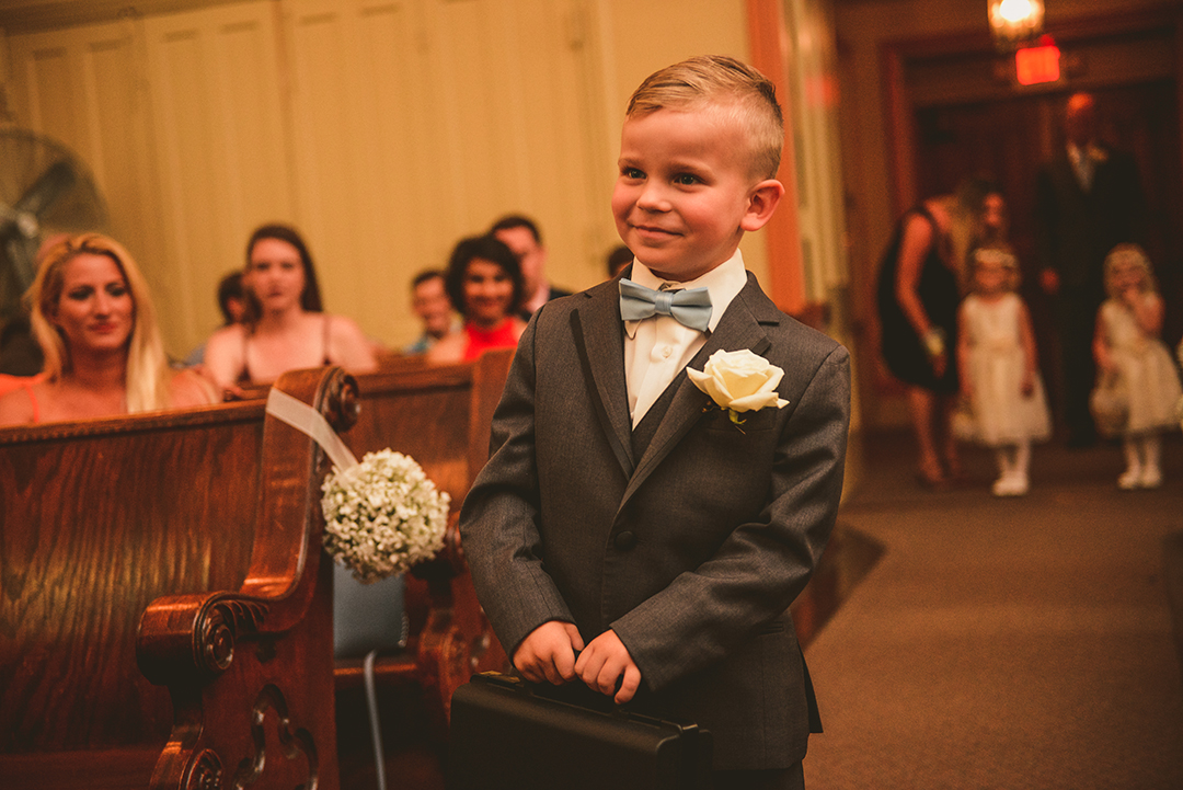 a ring bearer smiling as he walks down the aisle at a wedding