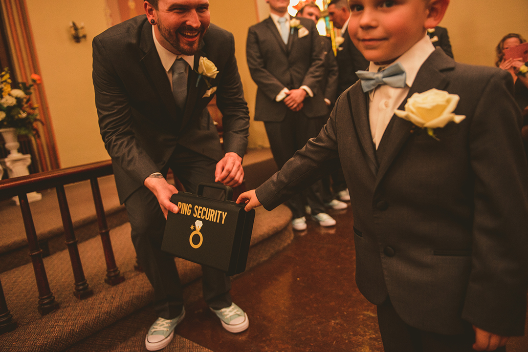 The ring bearer handing off a case that says ring security on it to a groom