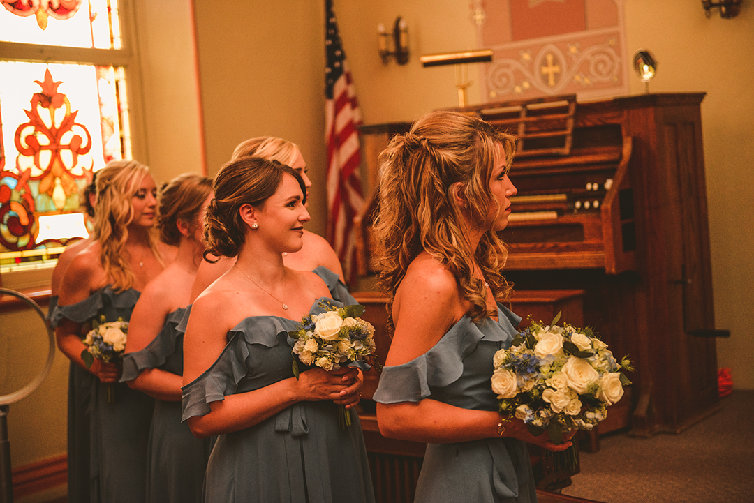 the bridesmaids smiling as they watch the bride and groom get married