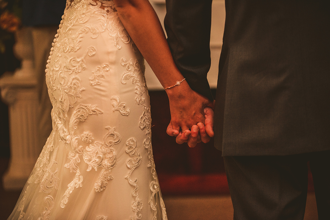 a detail of a bride and groom holding hands during their wedding ceremony