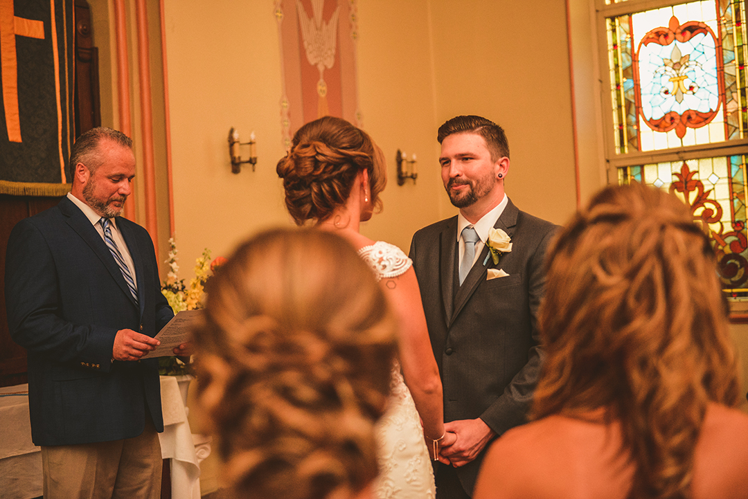 over a guests shoulder of a groom looking at his bride during his wedding ceremony