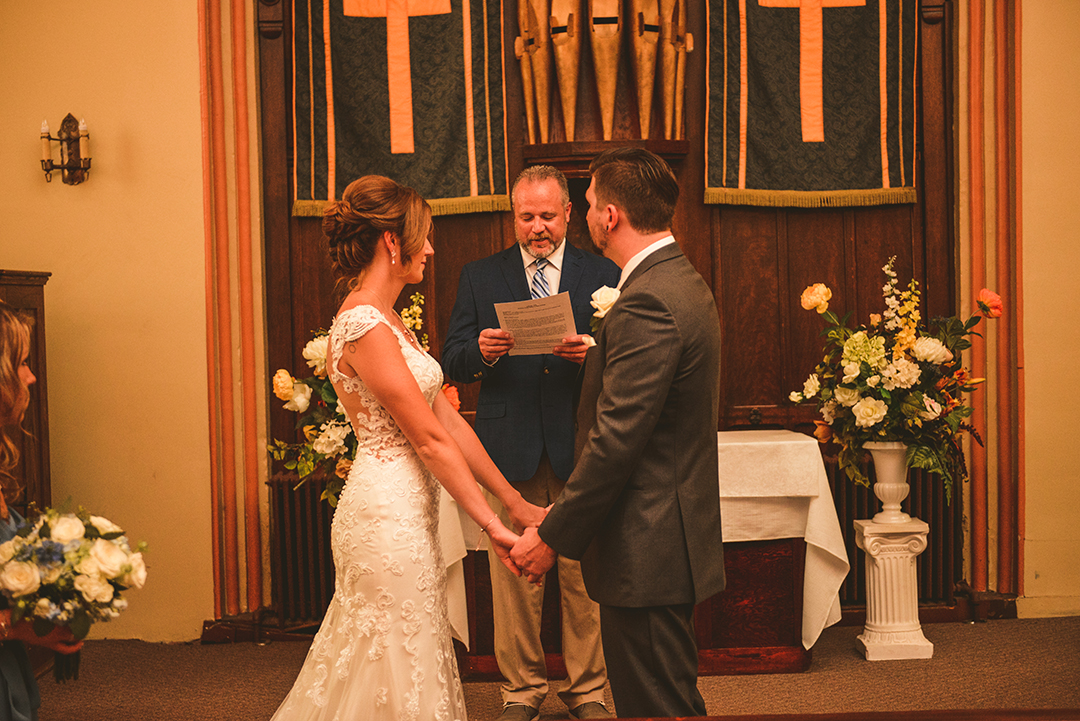 the bride and groom holding hands during their wedding ceremony at The Old Stone Church in Lockport