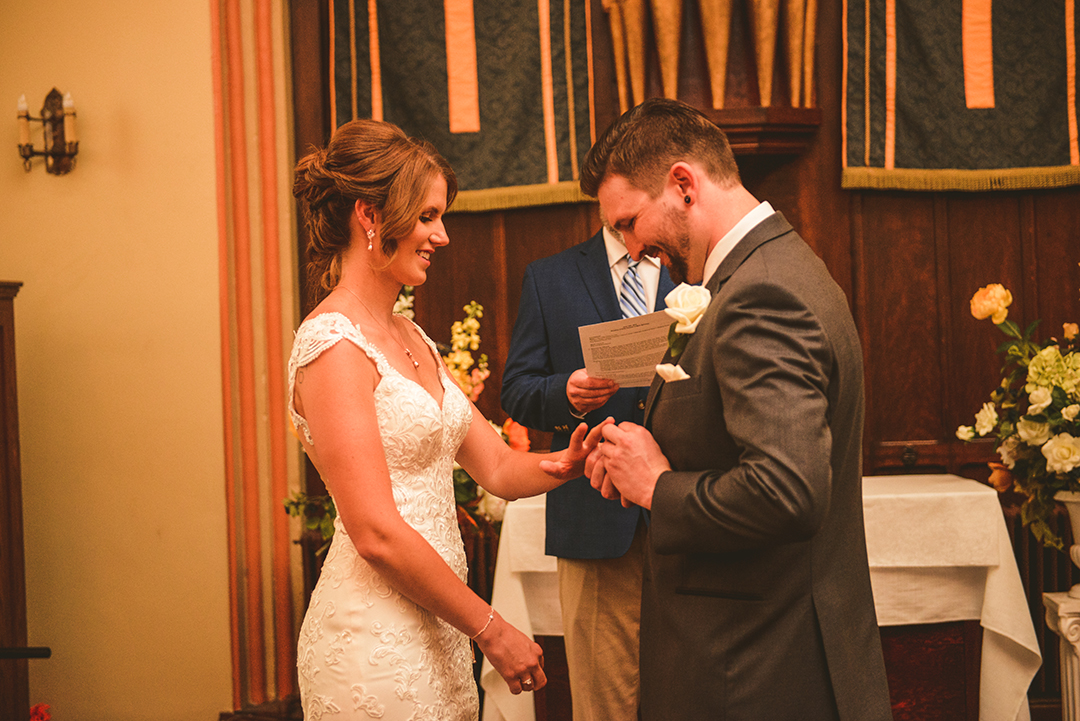 a groom placing a ring on his brides hand during their wedding ceremony in Lockport