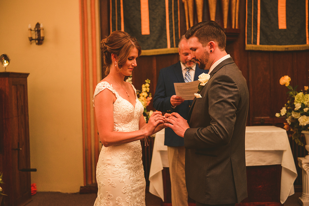 a bride placing a ring on her grooms hand at The Old Stone Church in Lockport