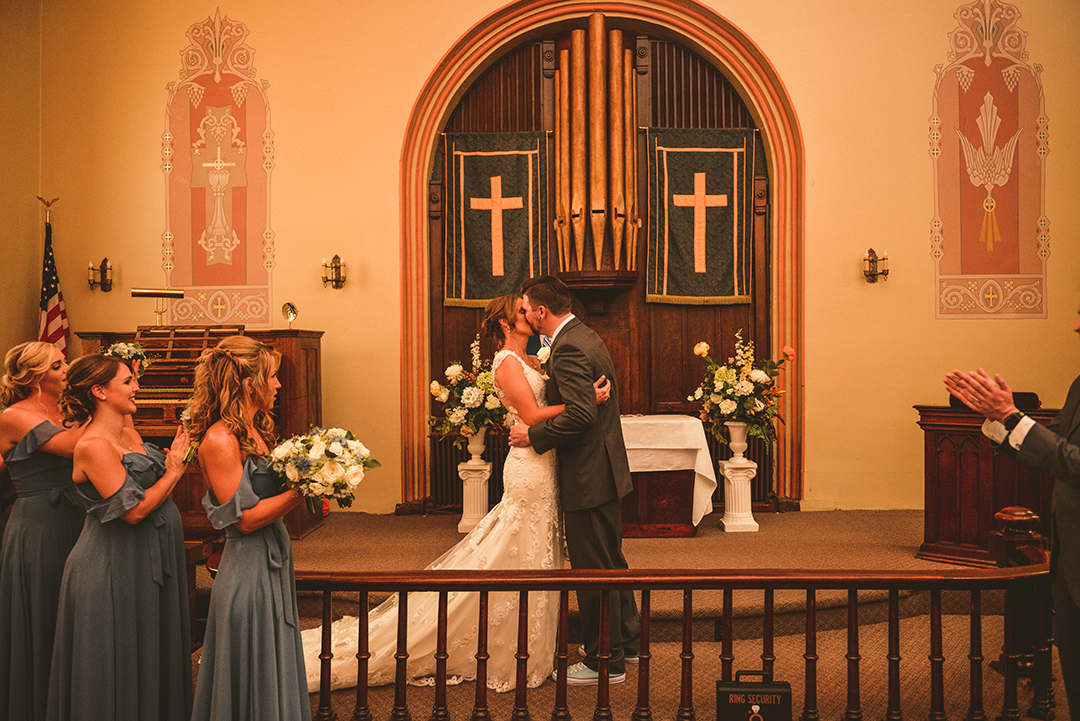 a bride and groom kissing for the first time on a church alter with an arch