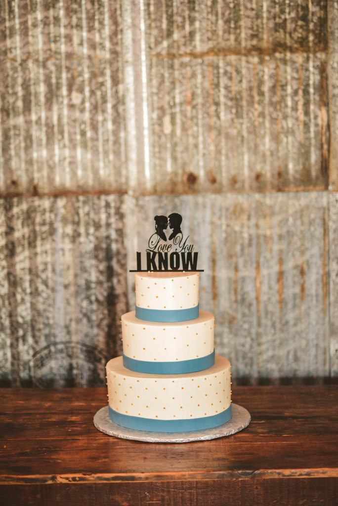 a wedding cake in front of silver metal siding with I love you, I know written on it