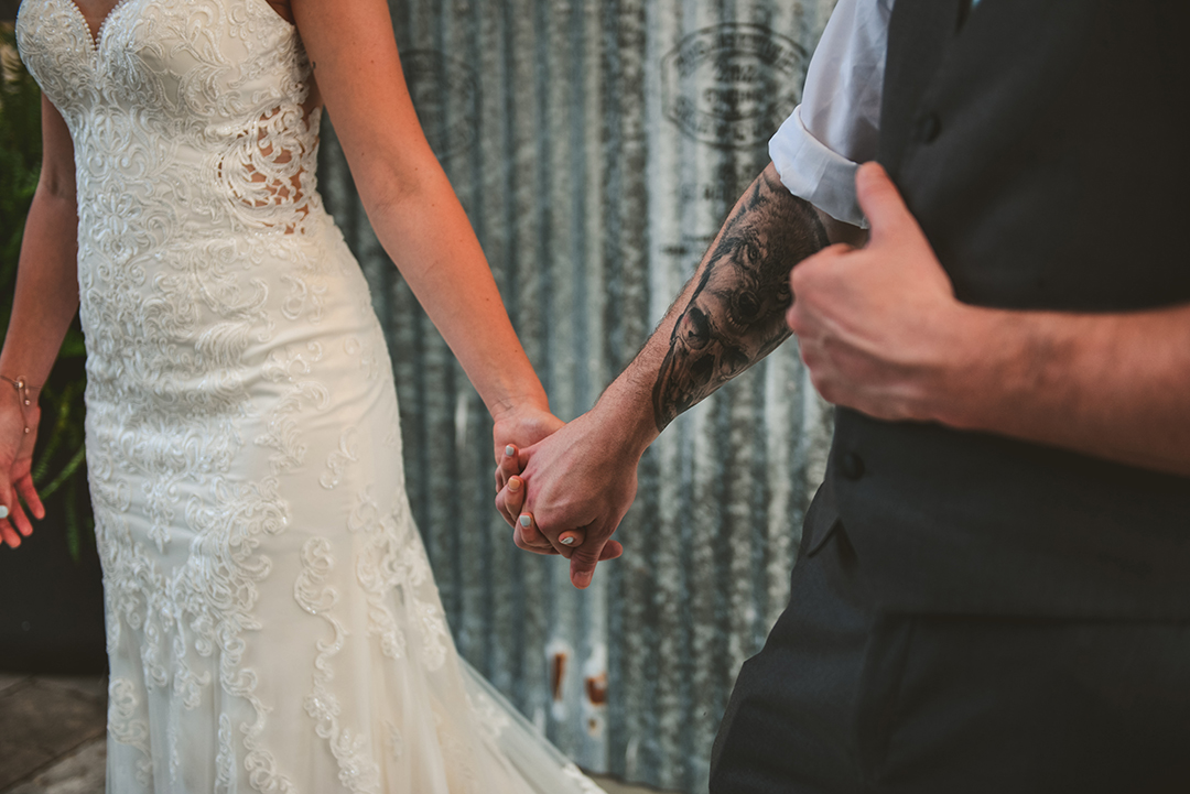 a tattooed groom holding his brides hand at Warehouse 109 in Plainfield