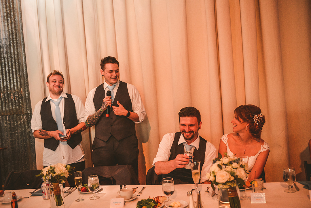 two groomsmen reading their speeches to the bride and groom