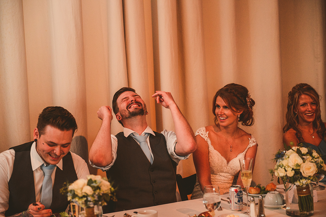 a groom laughing hysterically as the best man reads a speech at a wedding reception