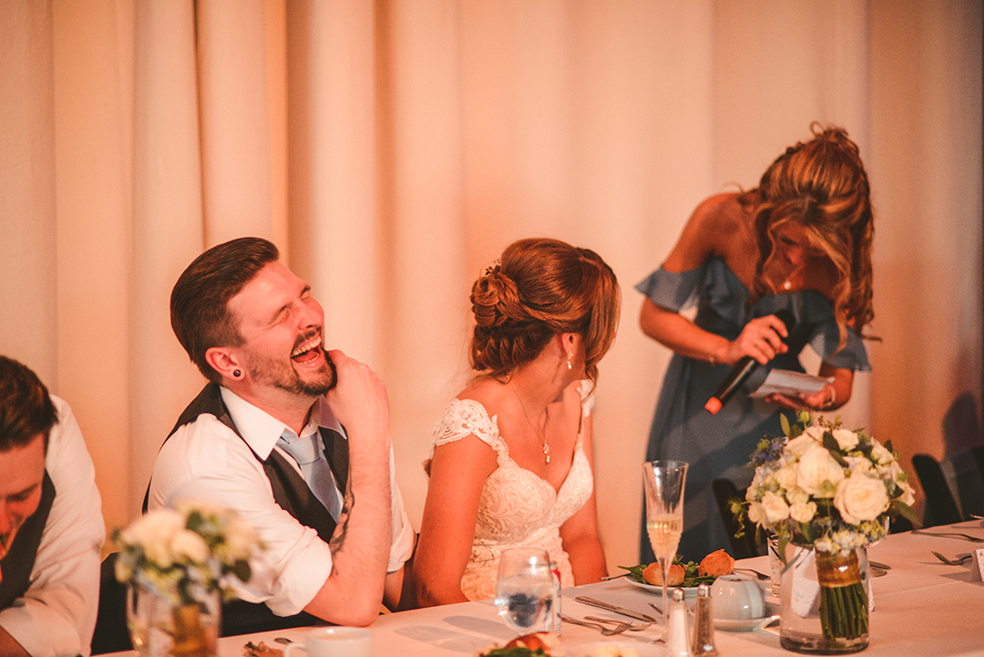 a groom laughing as the maid of honor reads her speech