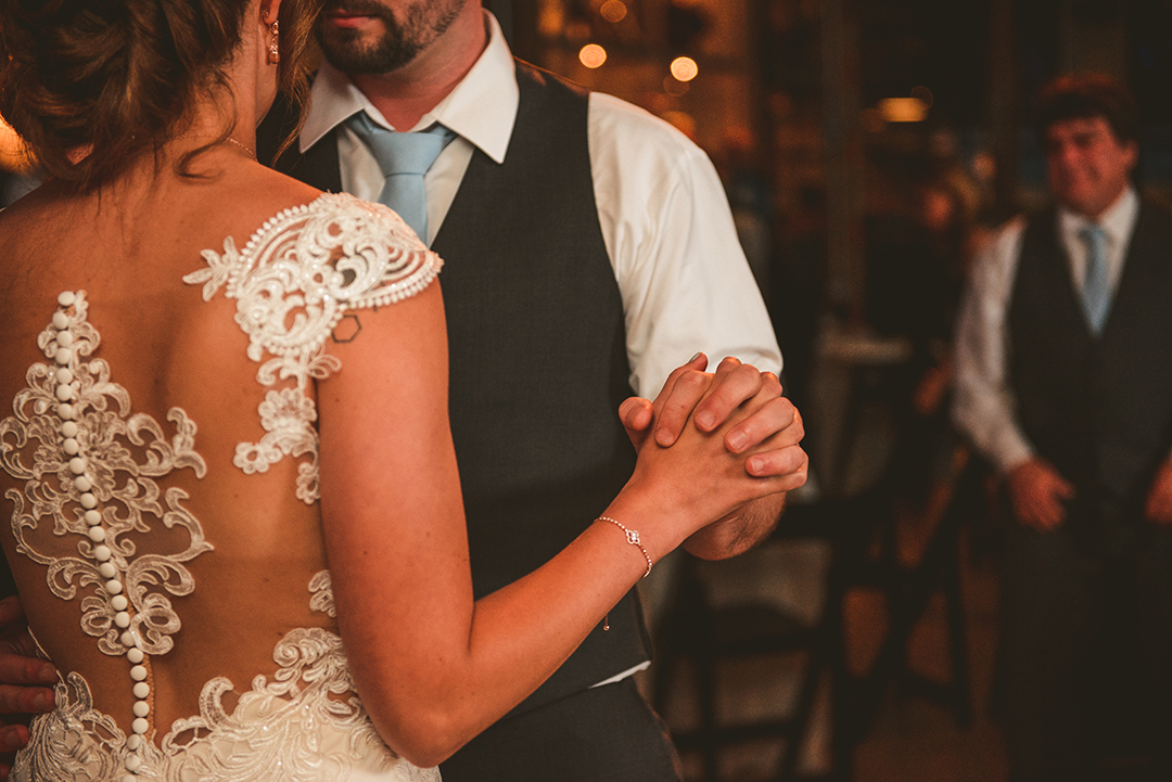 a detail of a bride and groom holding hands in warm light