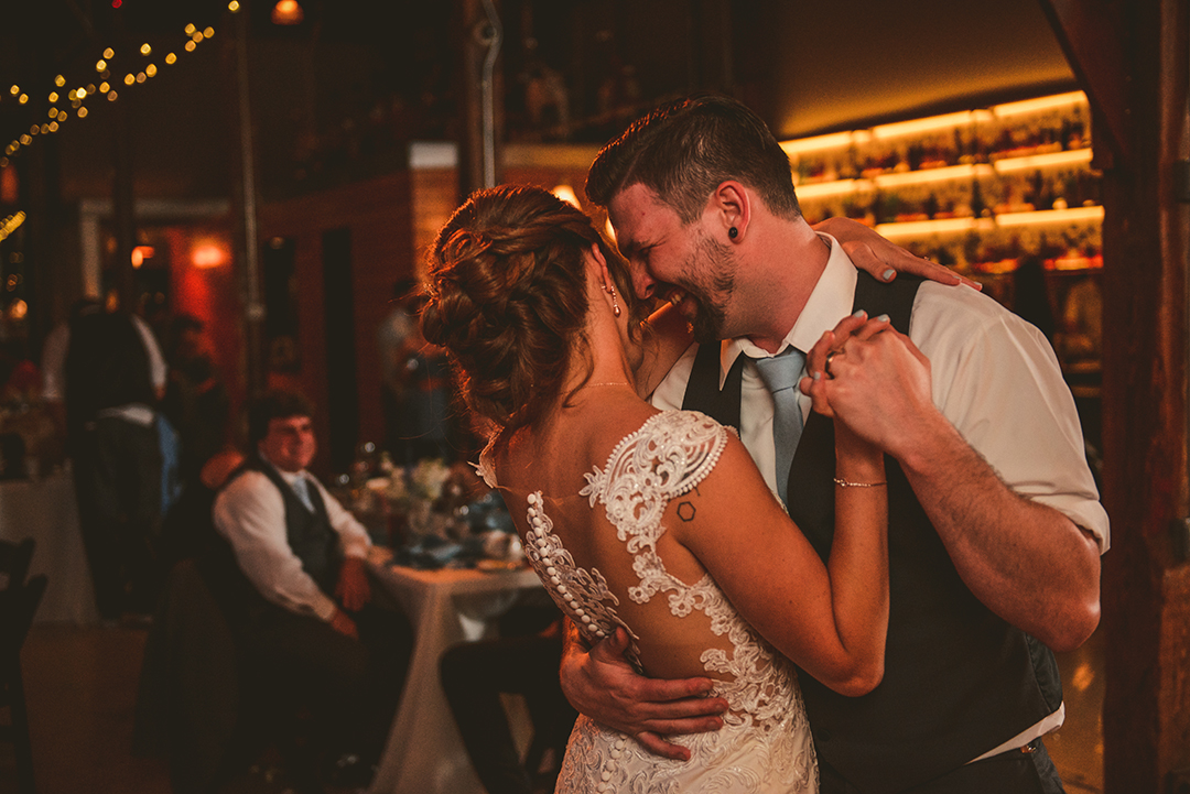 a bride and groom laughing during their first dance at a rustic wedding venue