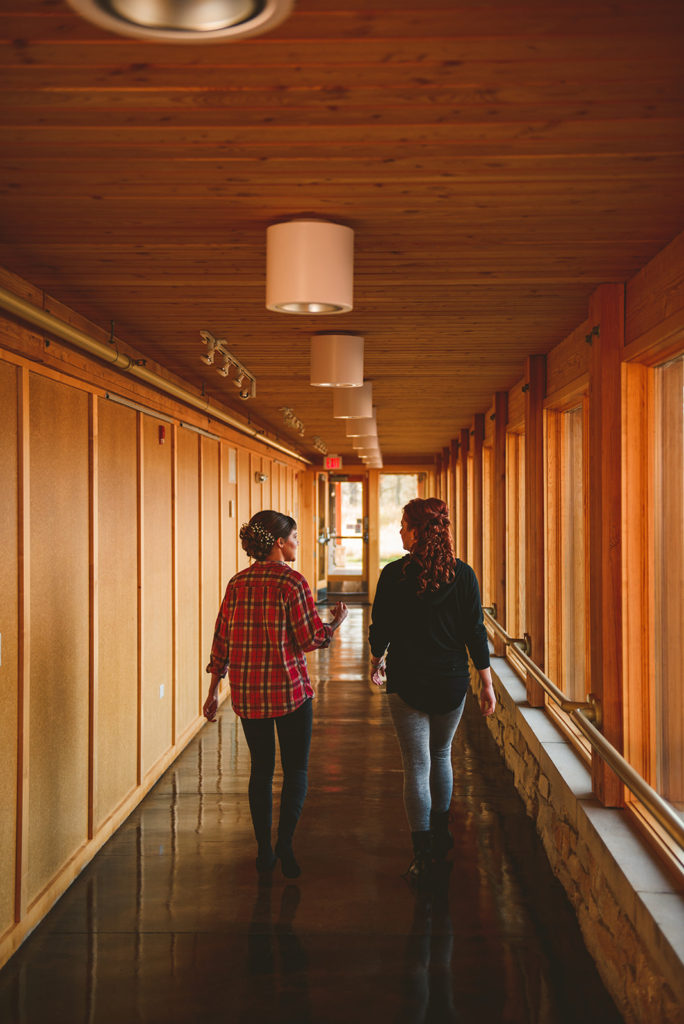 a bride and bridesmaid walking down a long hall way at the Four Rivers Environmental Education Center