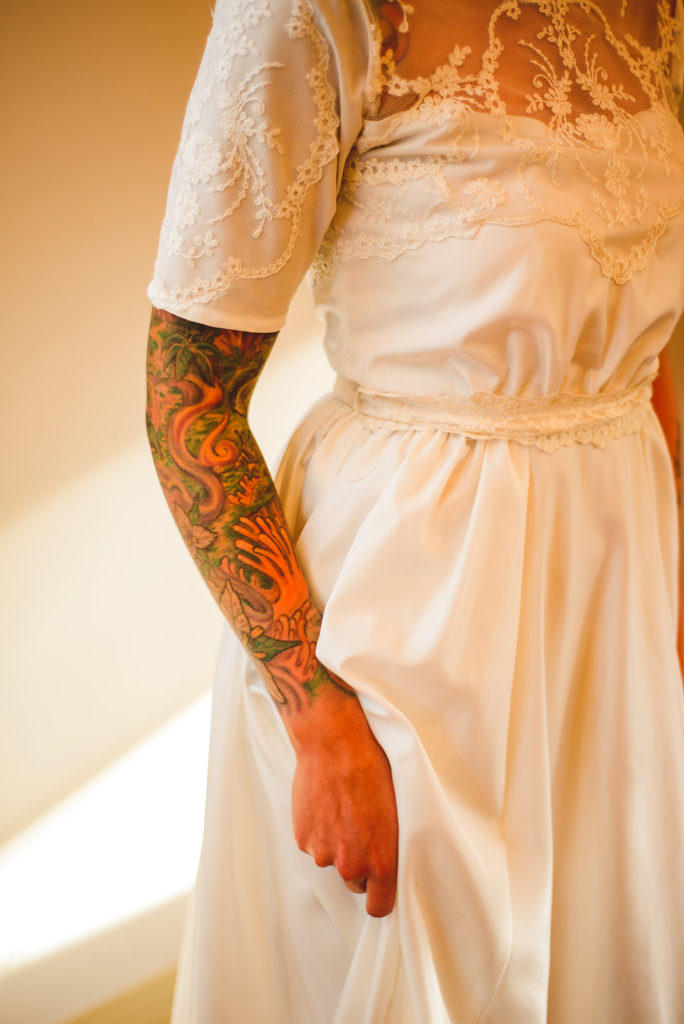 a tattooed bride holding up her train with strong backlighting