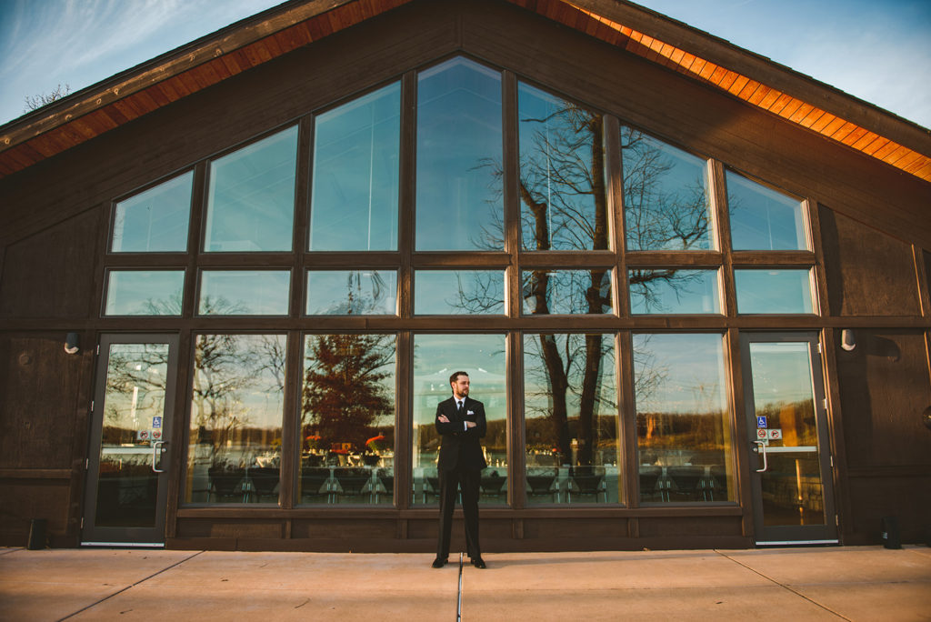 a groom standing in the back of the Four Rivers Environmental Education Center in Channahon with a clear blue sky