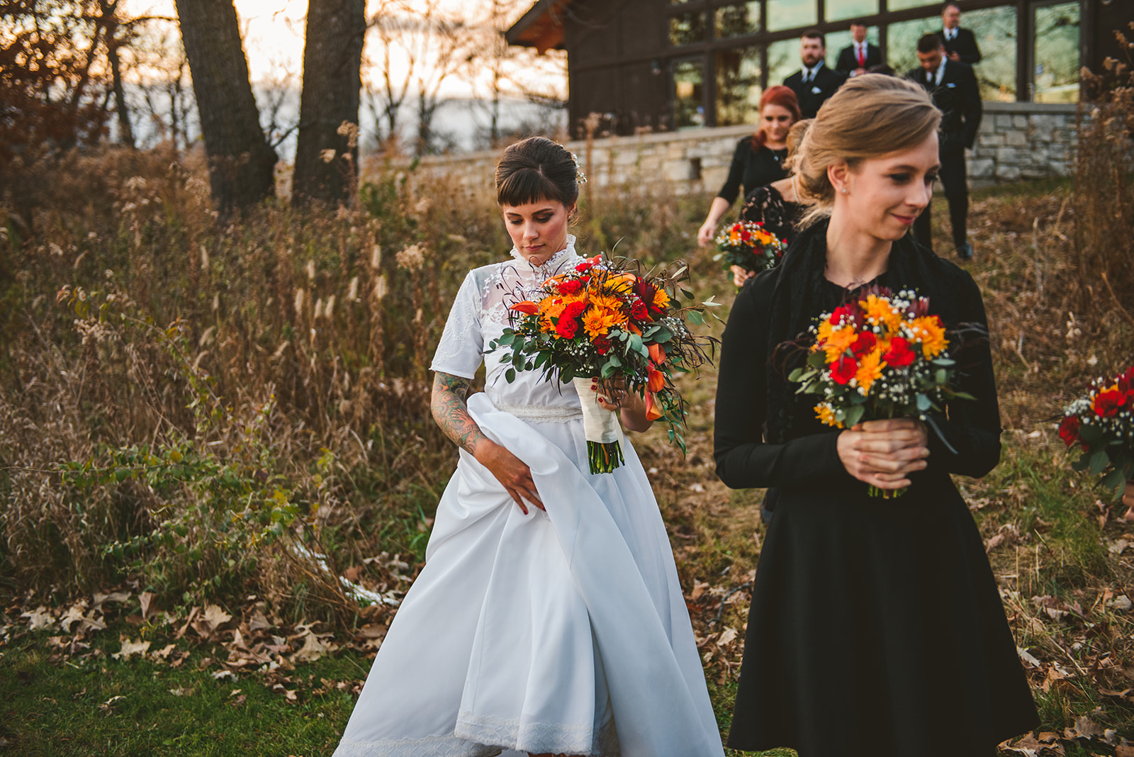 a bride holding her dress up as she walks through the grass in the evening at the Four Rivers Environmental Education Center