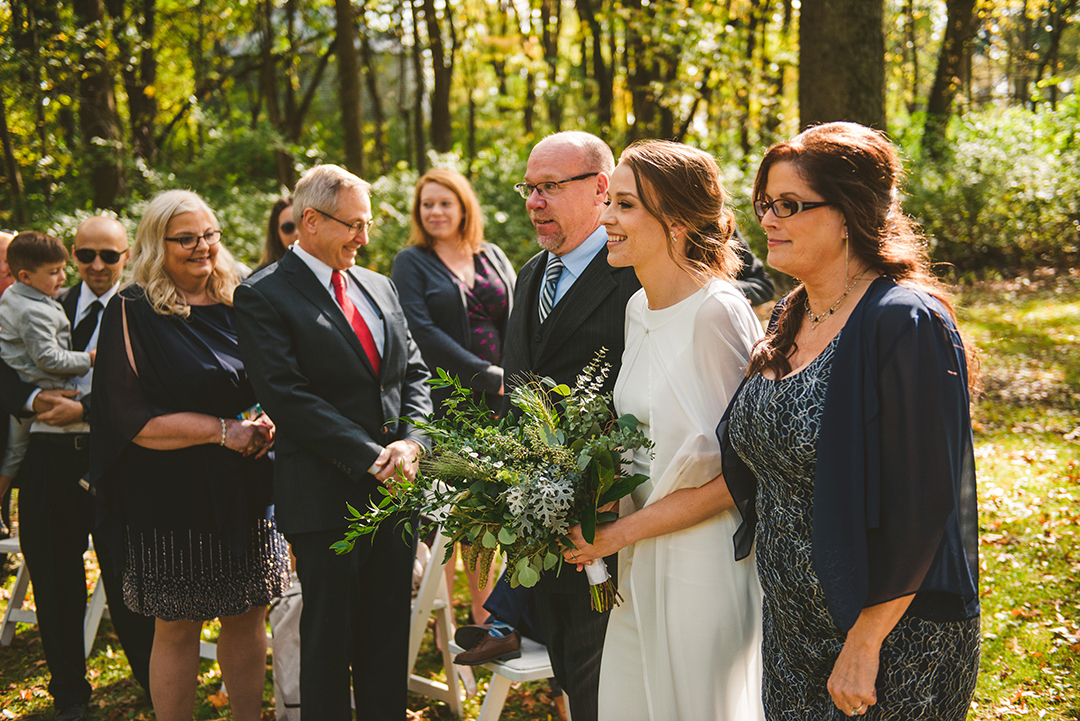 a mother and father walking their daughter down the aisle at a wooded wedding at the Saint James Farm in Warrenville IL in the fall as all their friends and family look on