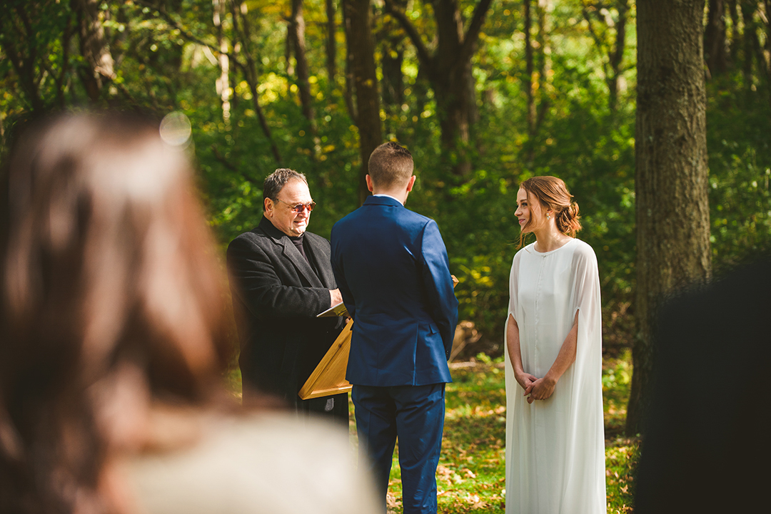 wedding guests looking on as a couple gets married at the Saint James Farm in Warrenville IL in front of large green trees in the fall