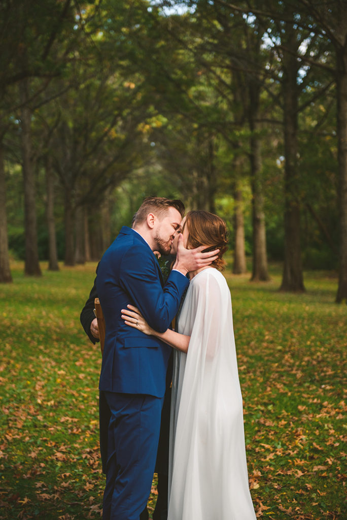 a groom and bride experiencing their first kiss by a row of trees at the Saint James Farm in Warrenville IL