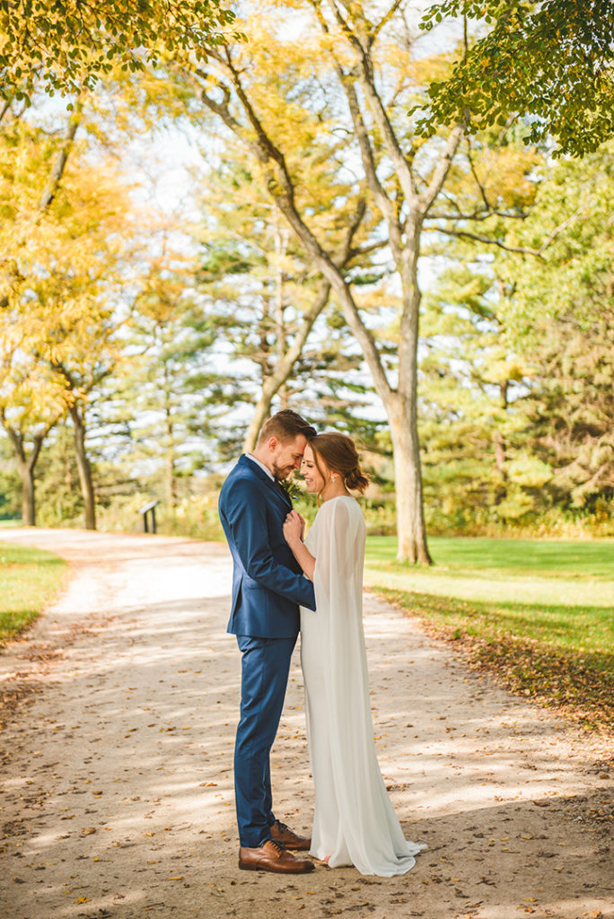 a bride and groom standing close while holding onto each other with fall colors around them at the Saint James Farm in Warrenville IL