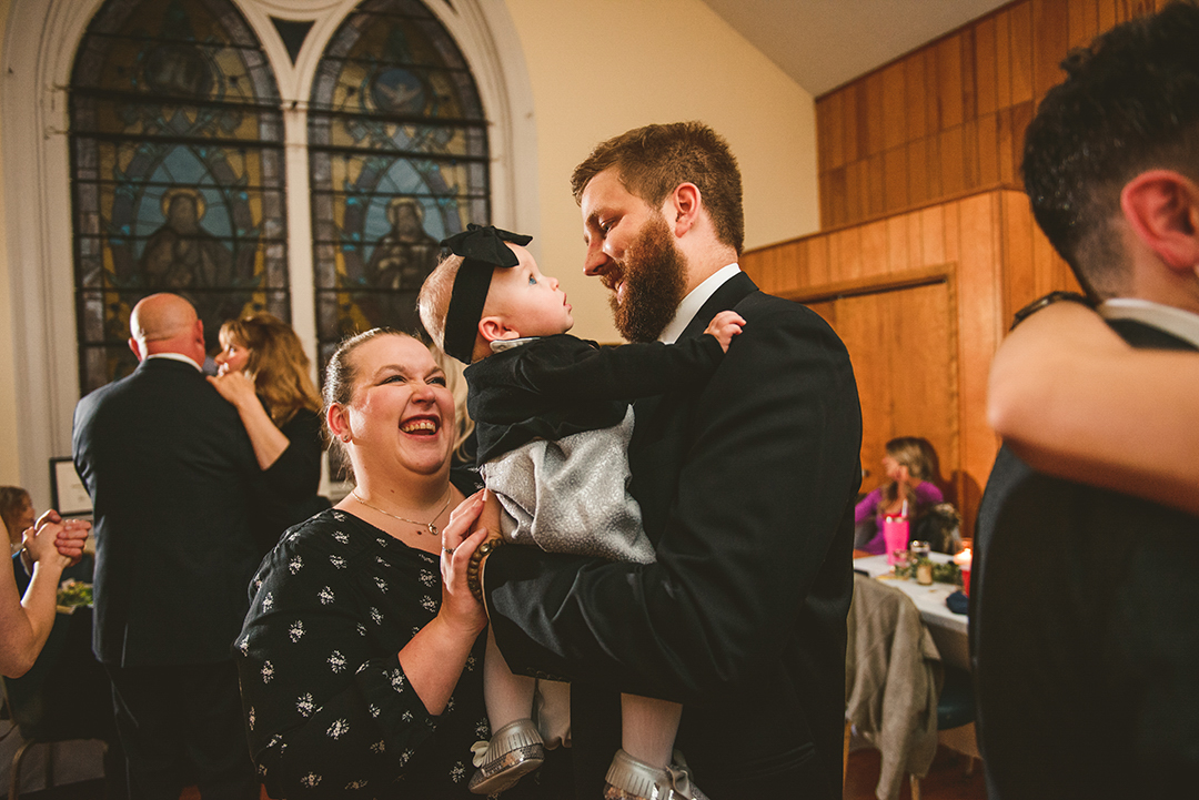 wedding couple dancing with their baby in front of stained glass windows in Naperville IL