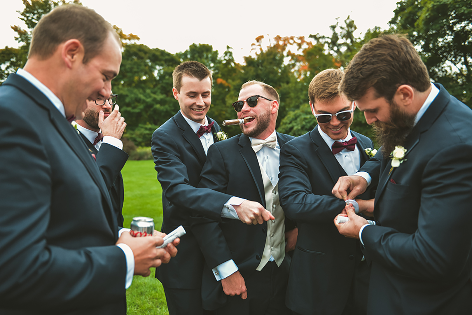 a groom and groomsmen smoking cigars at a Cantigny Park wedding as they all laugh in the fall weather