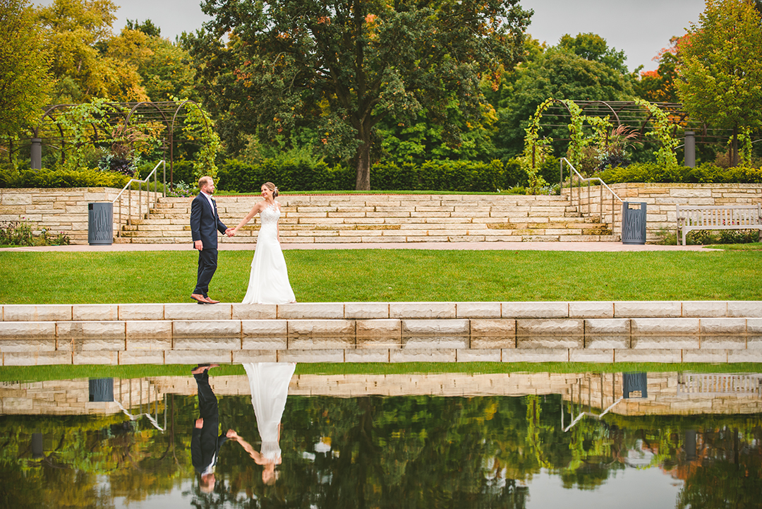 a bride leading her groom down a path at a Cantigny Park Wedding with their reflections in the water on a beautiful fall day