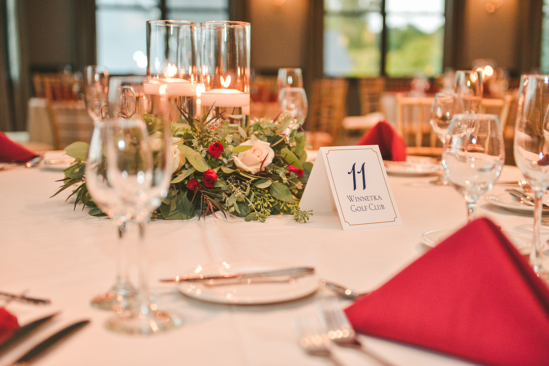 a close up of a place setting at the Cress Creek Country Club in Naperville with golden flickering candles and red napkins