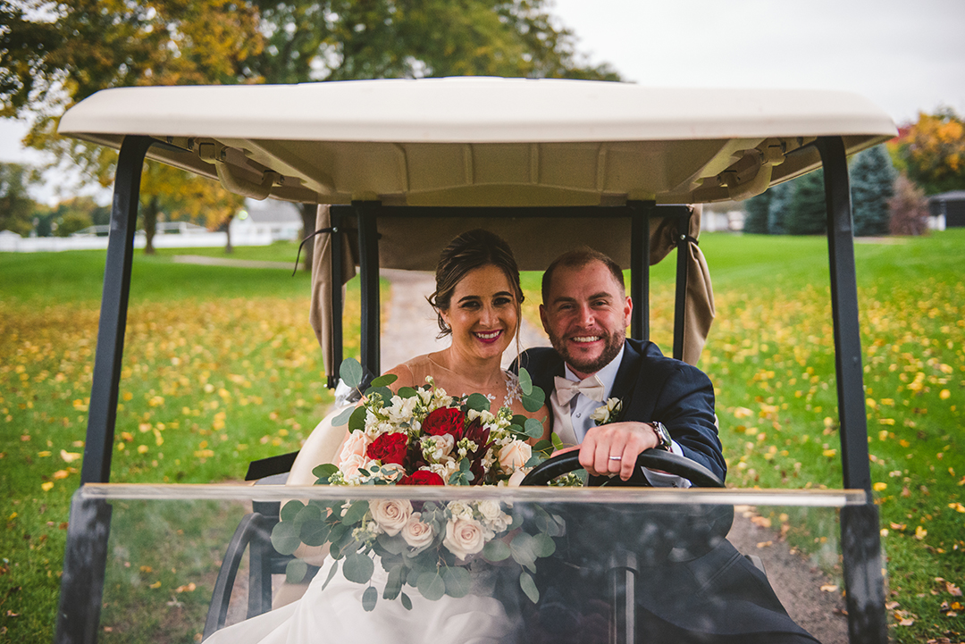 a bride and groom driving a golf car at the Cress Creek Country Club in Naperville as they smile on a fall day with their arms around each other